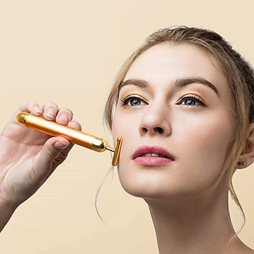 Woman using a gold facial roller on her face against a beige background