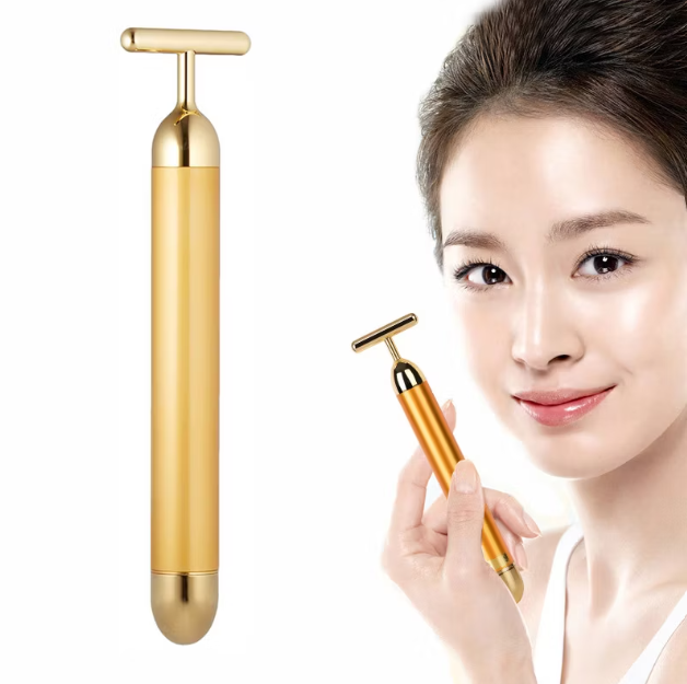Gold facial massager held by a person with a white background